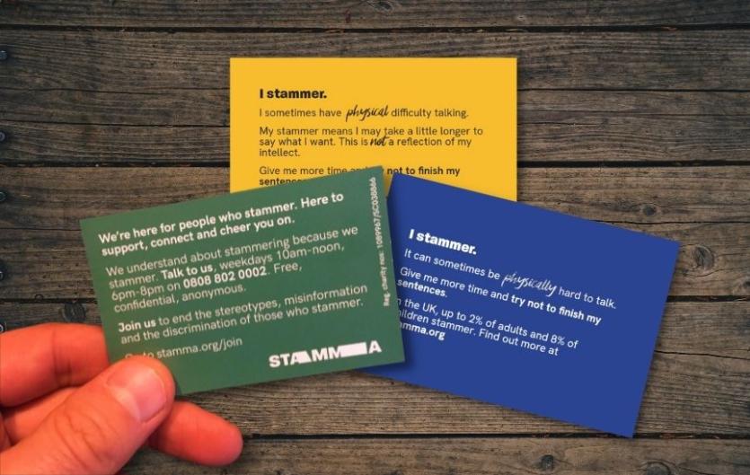 'I Stammer' Cards Three different coloured cards with text on them, and a hand holding one of them.