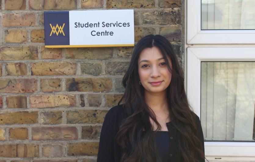 A woman standing by a wall, with a sign behind reading 'Student Support Service'