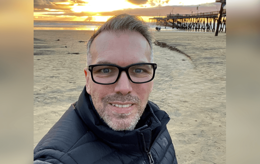 A man looking at the camera with a beach setting