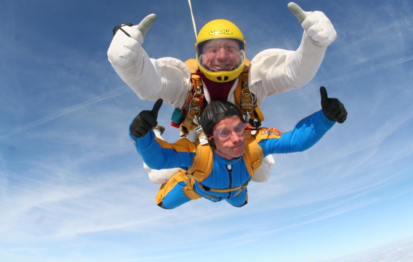 Two men tandem skydiving with their thumbs up