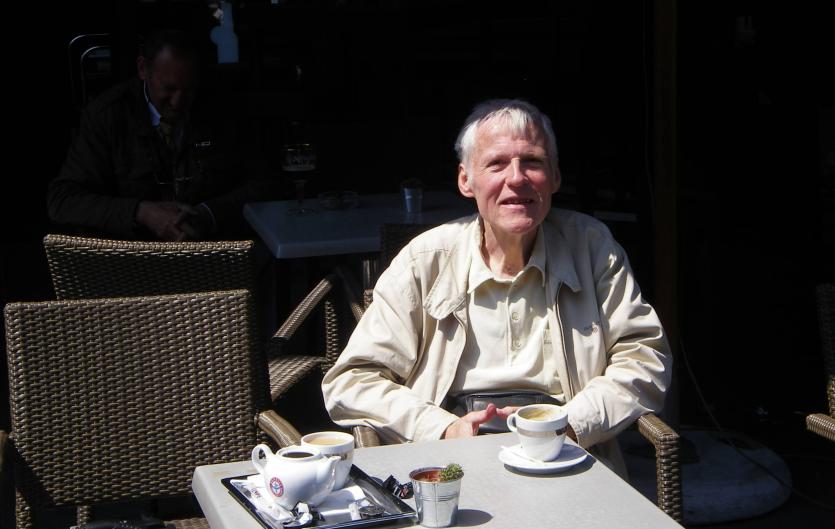 An elderly man sitting at a table and looking at the camera, smiling