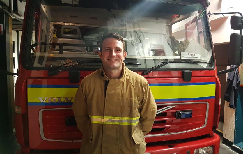 I could roar A man in a firefighting uniform standing in front of a fire engine and looking at the camera