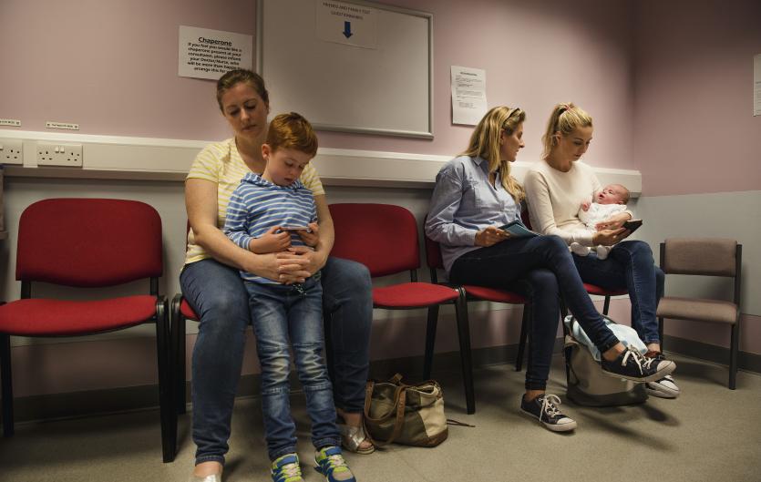 Mother with son in a clinic waiting room; therapist talking to another mother with a baby