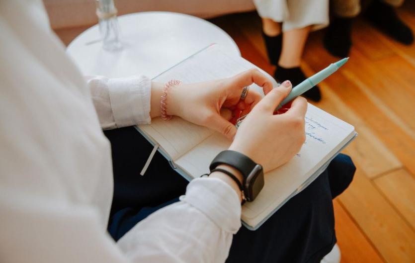 Speech & Language Therapy Peer Support Network A close up of a woman's hands holding a pen on top of a notebook, in a therapy room setting
