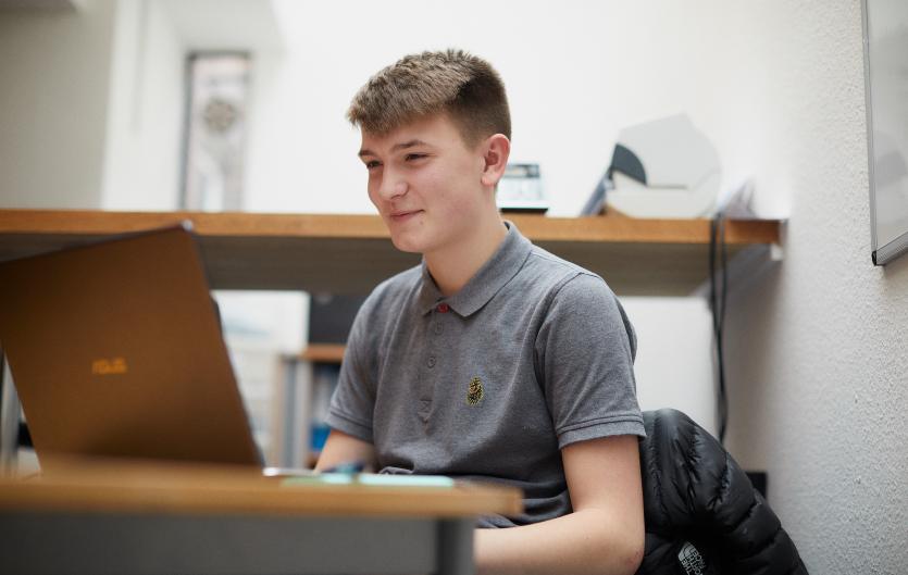 School Teenage boy working on laptop in a classroom setting