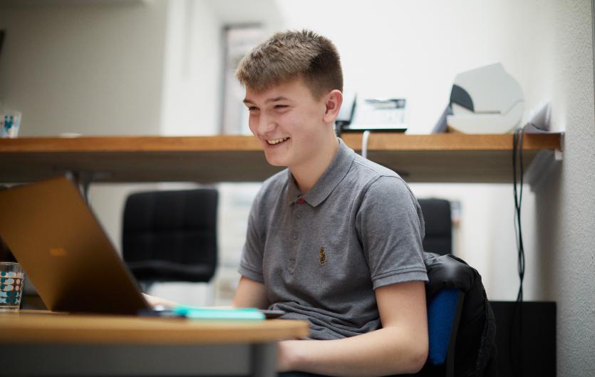 Options for Young People (13-17) A young man sat in front of a computer and laughing