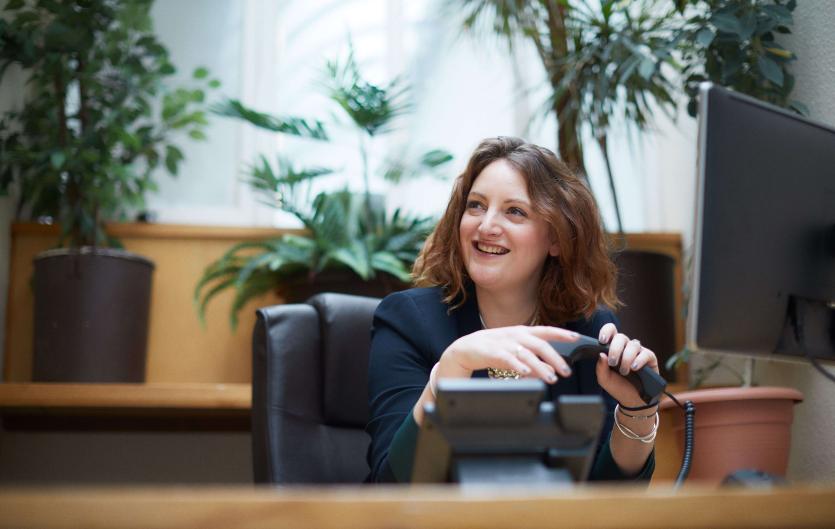 A woman at a desk making a telephone call and smiling at someone off camera