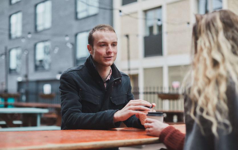 For Partners, Family & Friends A man sitting on a bench holding a coffee and chatting with a woman