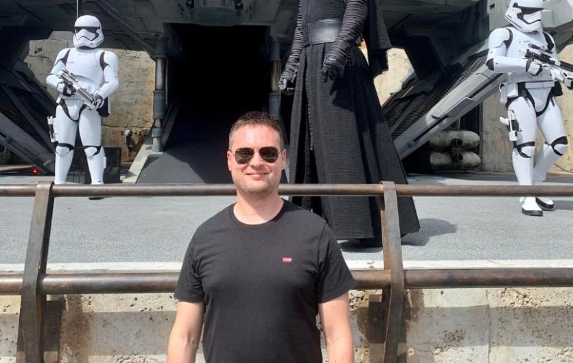 Media representation is important A man looking at the camera and smiling, with life-size model figures from Star Wars behind him