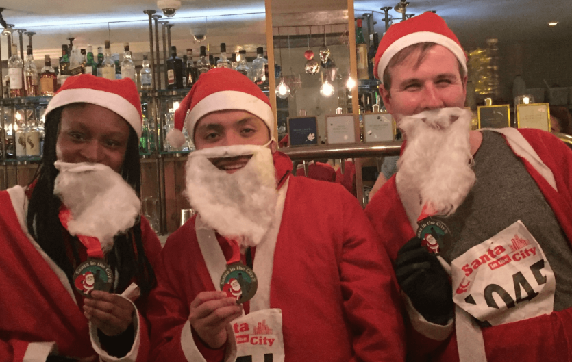 Three people dressed as Father Christmas holding medals and looking at the camera