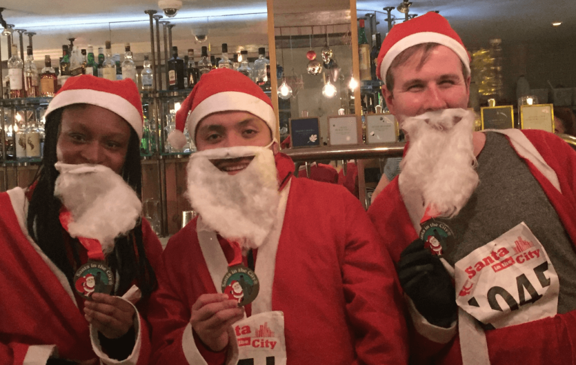 Santa In The City 2021 Three people dressed as Father Christmas holding medals and looking at the camera