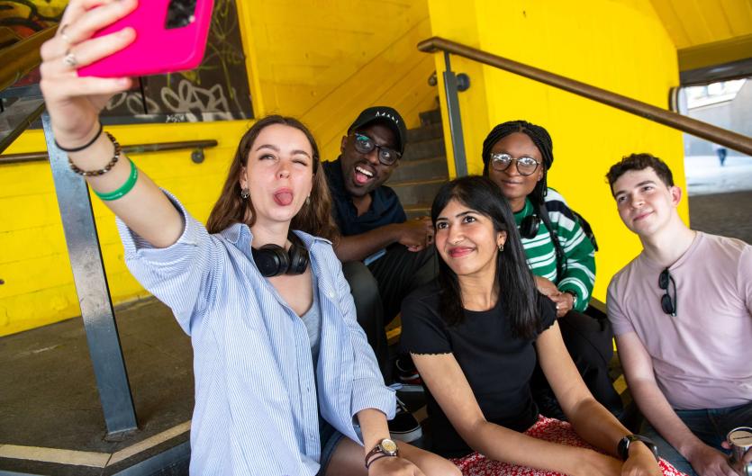 Impact A group of young people posing for a selfie photo with one woman holding a phone
