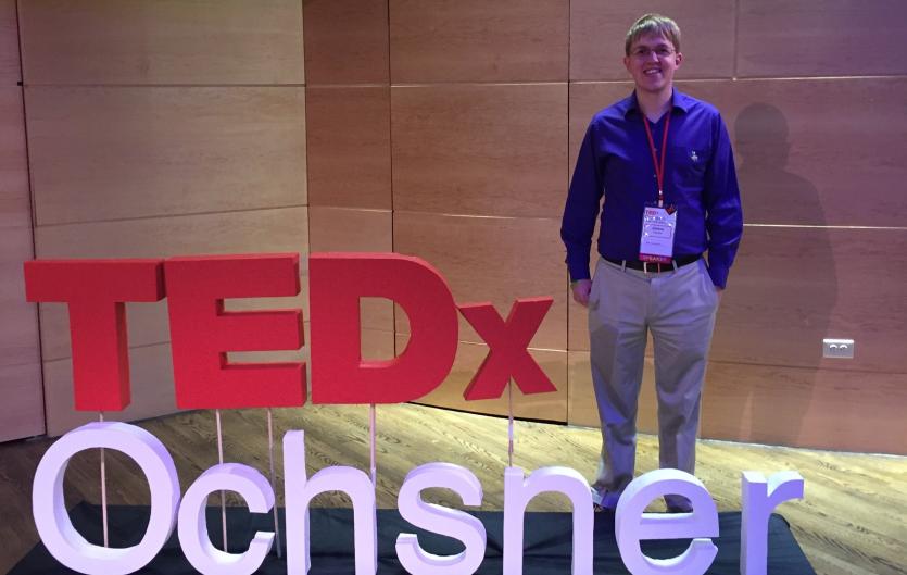 James Hayden at a TED talk, with a sign saying: 'TEDx Ochsner'