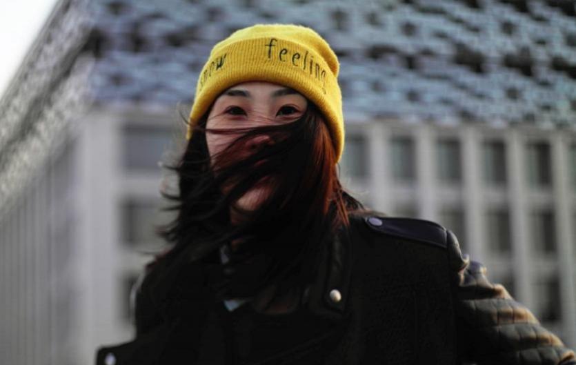 A lady in a yellow woolly hat looking at the camera with her hair covering her face