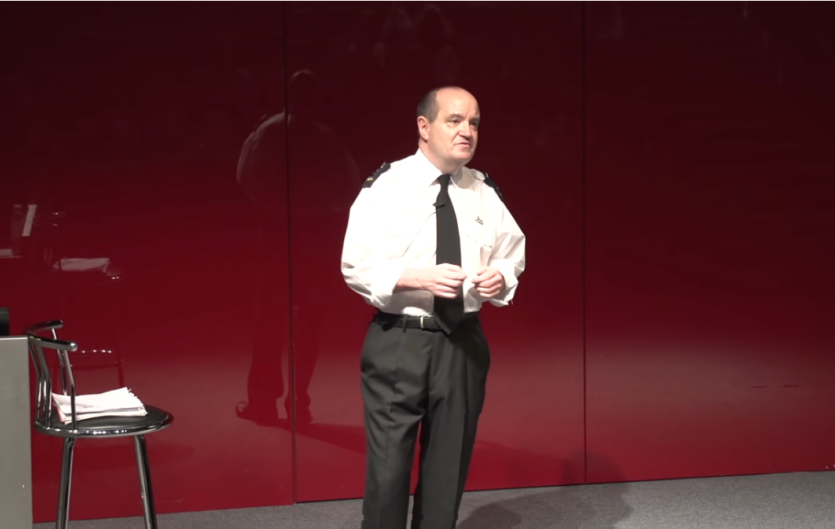 Brian Skelton speaking onstage in security guard's uniform