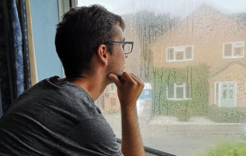 A man looking out of the window and looking thoughtful, with his head in his hands