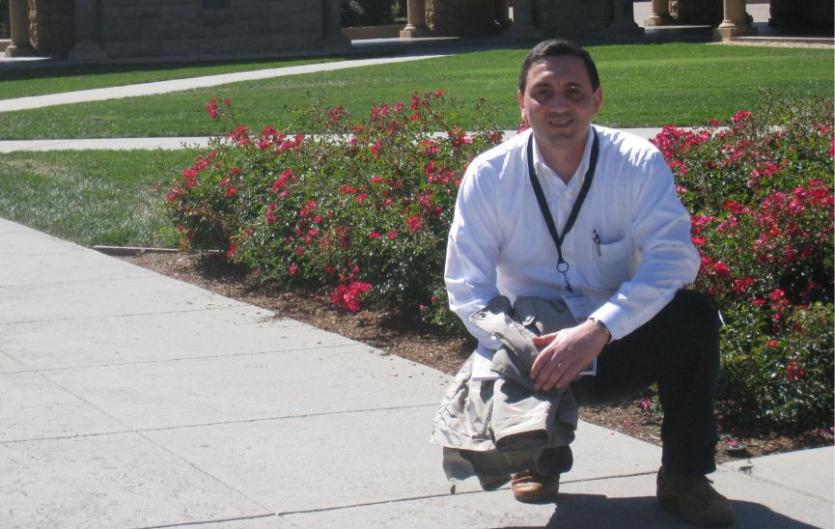 A man kneeling in front of a flowerbed, and looking at the camera