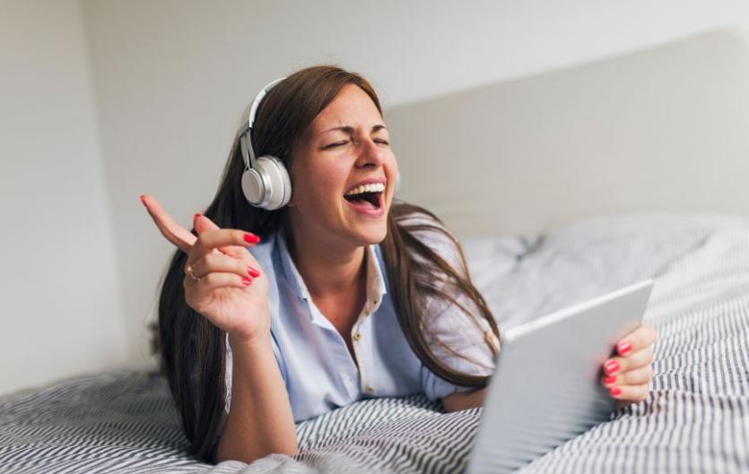 Take part in a singing and voice confidence study A woman wearing headphones and singing in front of a laptop computer