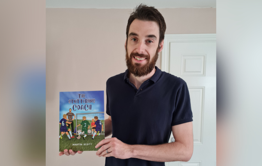 Writing my book 'The Stuttering Coach' A man looking at the camera, holding a book