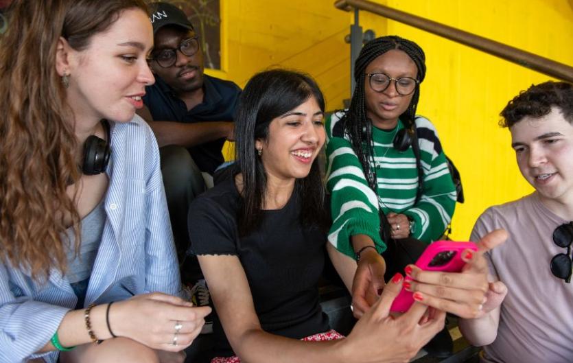 A group of young people looking at a mobile phone that one of them is holding, and smiling