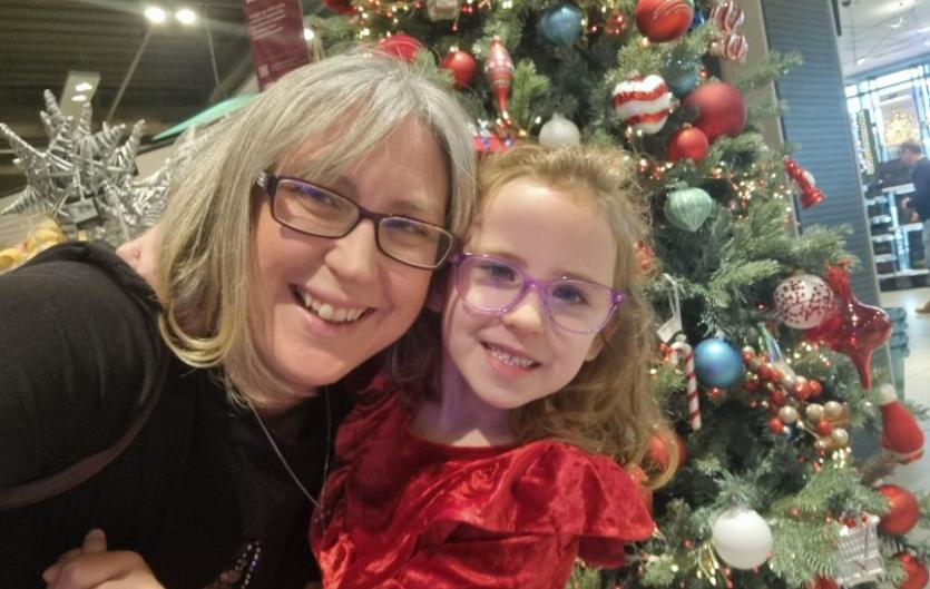 Making the Christmas magic easier for Jasmine this year A woman and her young daughter looking at the camera and smiling, with a Christmas tree in the background.