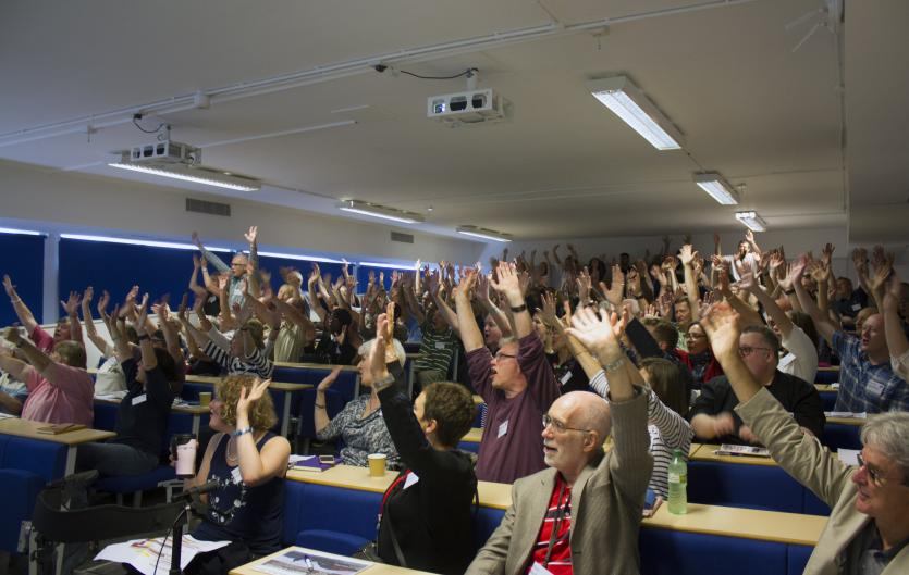 A packed lecture hall, people raising hands to vote; Cardiff Conference 2018