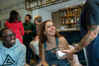 A young man and woman in a cafe looking at a waitress and holding a mobile phone to a card reader