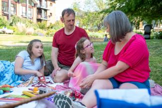 A family picnic, with a young girl speaking and her mother, father and daughter sitting listening to her