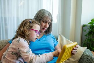 A mother and young daughter sitting on a sofa and looking at a tablet