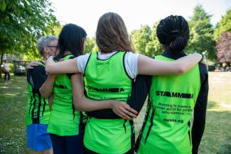 A man and three women in running vests linking arms with their backs to the camera