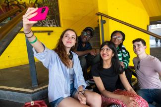 Three women and two men sitting and posing for a selfie photo from a phone held by one of the women