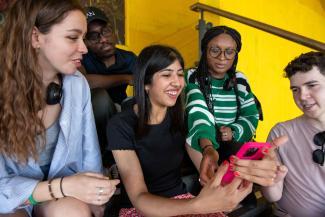 Three women and two men sitting together and looking at a mobile phone being held by one of the women