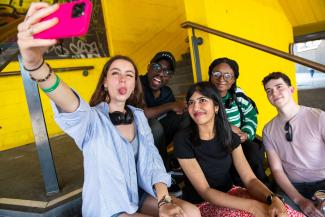 Three women and two men sitting and posing for a selfie photo from a phone held by one of the women
