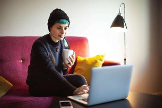 A woman sitting on a sofa and typing on a laptop in front of her on a coffee table