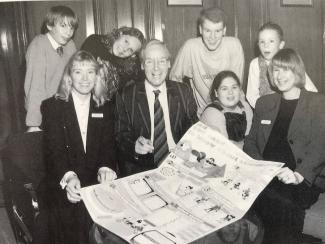 A group of children and adults smiling for the camera whilst holding and displaying a poster