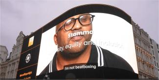 An advertising screen in Piccadilly Circus displaying a man looking at the camera, with the words 'Stamma' on it