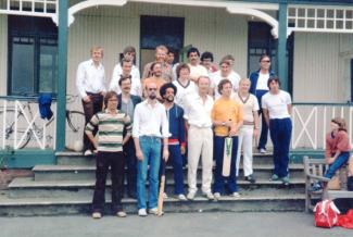 A group of men standing in front of a cricket pavilion, looking at the camera