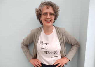 A woman with her hands on her hips, smiling for the camera. She is wearing a t-shirt that reads 'Please don't interrupt'.