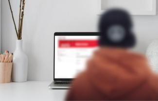 A blurred person sitting in front of a laptop computer on a desk. The screen is blurred too