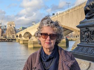 A woman standing by the River Thames, smiling for the camera