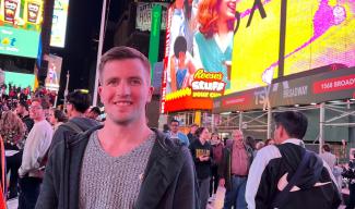 A man in a city setting looking at the camera and. Around him are people walking in the city