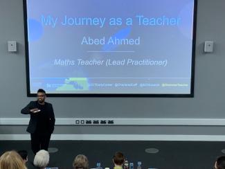 A man presenting to an audience, standing in front of a projector screen