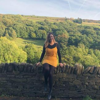 A woman sitting on a wall in the countryside, looking at the camera