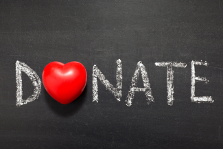 Donate written in chalk on a dark board with a red heart over the 'O'