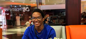 A young man sitting in an indoor public place, smiling for the camera