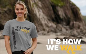 A woman standing on a beach looking at the camera. Next to her are the words 'Its how we walk'