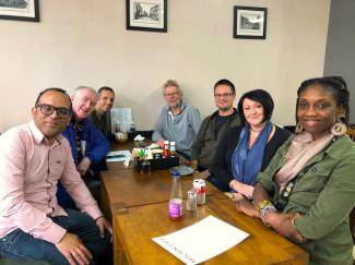 Seven people sitting around a cafe table smiling for the camera