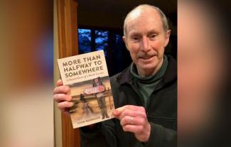 A man holding a book up and smiling for the camera