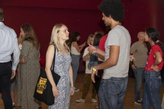 A young woman and young man chatting with lots of people chatting around them