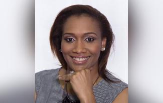 A woman smiling at the camera with her head resting on her hand